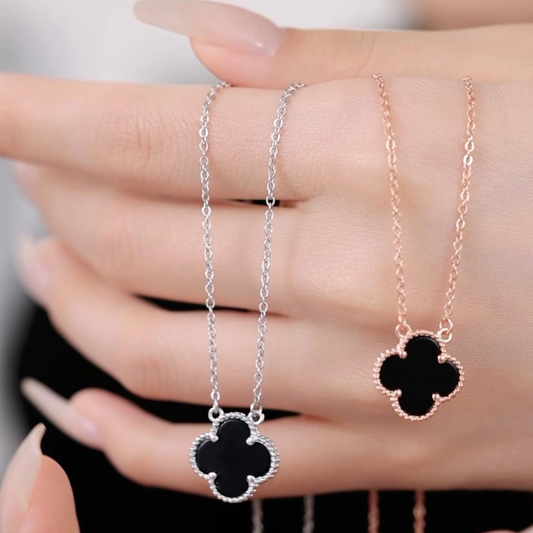 A hand holding the Black Flower Elegance Necklace, featuring a black flower pendant on a silver chain.