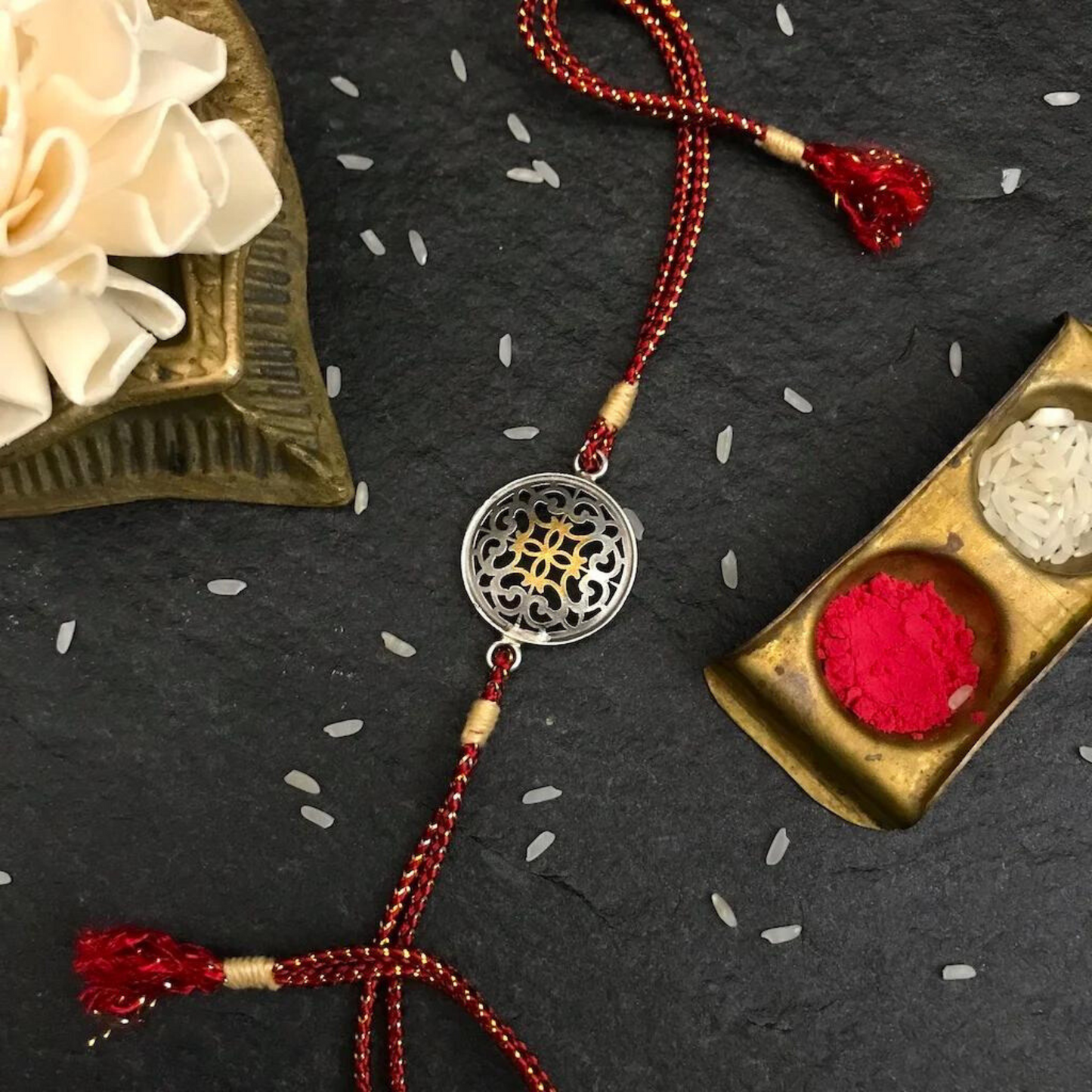 Elegant Filigree Rakhi with Red and Gold Threads featuring intricate filigree detailing, a central flower design, and woven luxurious threads, symbolizing sibling love and protection.