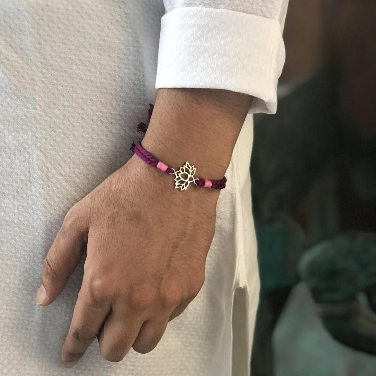 A person wearing Bliss Jouels' Handcrafted Lotus Rakhi with maroon and pink threads, featuring a delicate lotus charm.