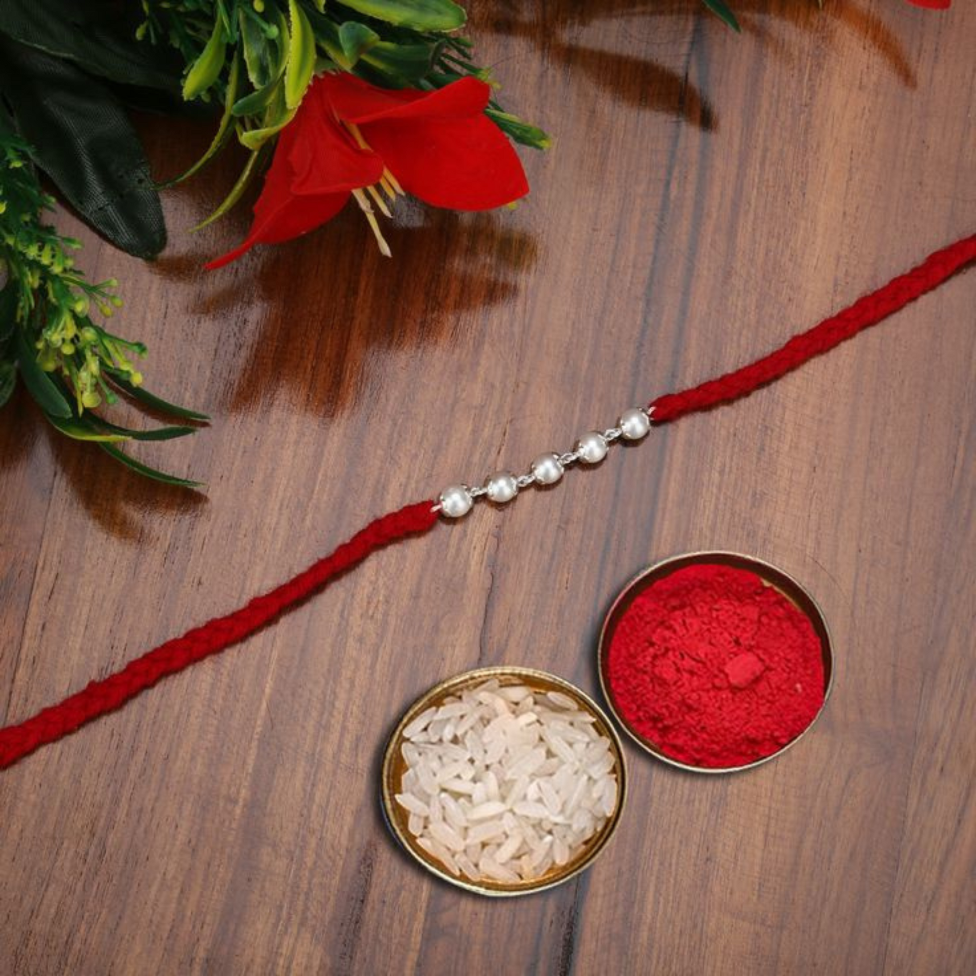 Bliss Joule's Traditional Red Threaded Rakhi with Silver Accents, paired with bowls of rice and red vermilion powder for Raksha Bandhan rituals.