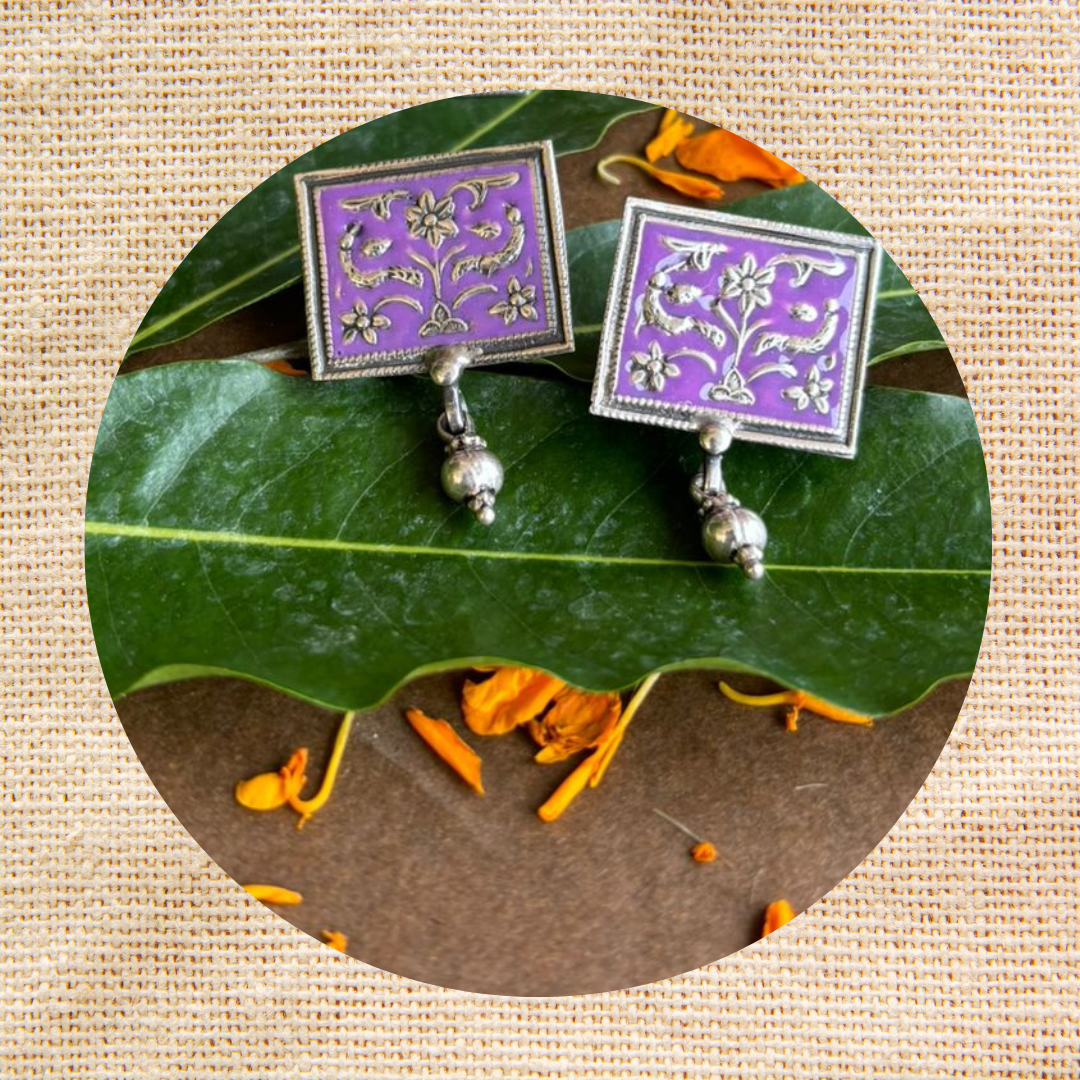 A pair of Bliss Old World Charms Earrings displayed on a leaf, showcasing their intricate design and vintage-inspired sophistication.